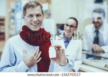Happy Healthy Man Holding Bottle with Pills. Pharmacists Standing at Counter. Pharmacists Looking at Man. Pharmacists is Wearing Special Medical Uniform. People Located in Pharmacy.