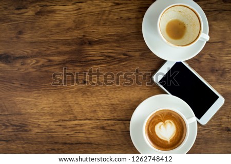 Cup of coffee with heart pattern in a white cup and smart phone on wooden background, Top view, Ideas for doing business online