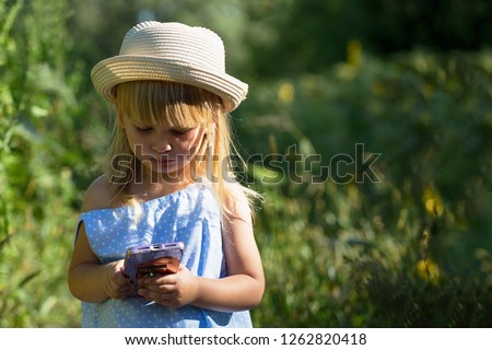 Little girl use phone on field. Summer sunny day.