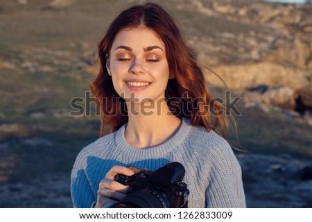 happy red-haired woman in a sweater and with a camera in nature                             