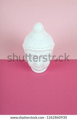 a white porcelain bouddha head on a pink and vibrant background. Minimum color still life