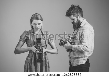 Man and woman on strict faces on grey background. Vintage photography concept. Man in checkered clothes, retro style. Company of busy photographers with old cameras, filming, working