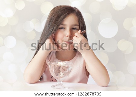 Happy child girl eating ice cream in white and chocolate bowl on light background. Enjoying delicious.