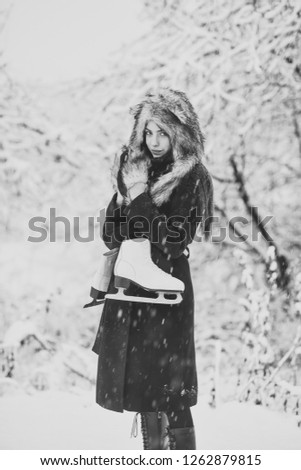 Girl with pair of figure skates at trees in snow. Woman with skating shoes in winter clothes in snowy forest. Ice skating concept. Sport, activity, health. Vacation, holidays, hobby, lifestyle.