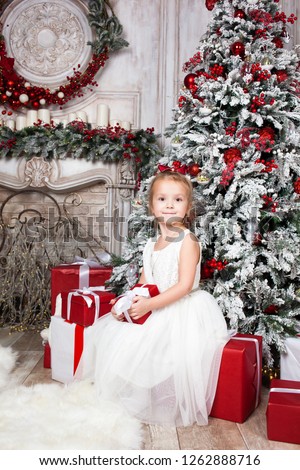 Happy little girl with toys and presentsat home sitting near Christmas tree. Happy Family concept