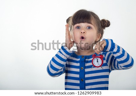 Surprised girl in dress with red clock on white background. Shocked kid holding alarm clock.