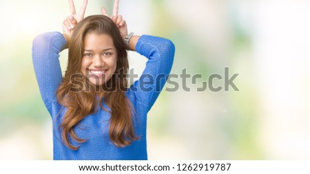 Young beautiful brunette woman wearing blue sweater over isolated background Posing funny and crazy with fingers on head as bunny ears, smiling cheerful