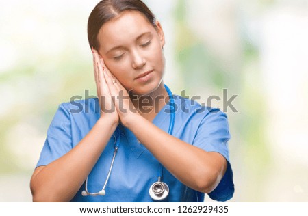 Young caucasian doctor woman wearing medical uniform over isolated background sleeping tired dreaming and posing with hands together while smiling with closed eyes.