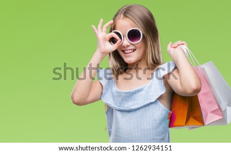 Young beautiful girl holding shopping bags on sales over isolated background with happy face smiling doing ok sign with hand on eye looking through fingers