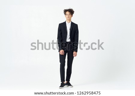 Curly business man in a black suit stands on a light background                    