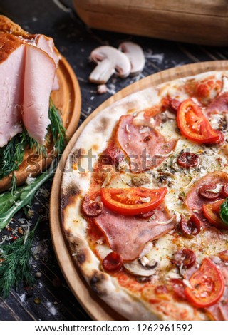 Pizza with sausages, ham, mushrooms and tomatoes. Background ready for your design. Pizza on a black background