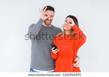 Young couple using smartphone over isolated background with happy face smiling doing ok sign with hand on eye looking through fingers