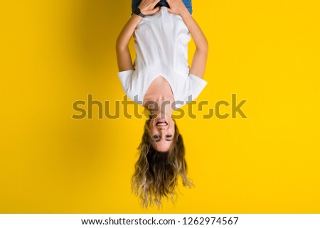 Beautiful young blonde woman jumping happy and excited hanging upside down over isolated yellow background Royalty-Free Stock Photo #1262974567