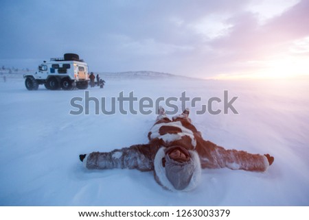Young man lying on snow dressed in Nenets warm clothes at sunset, in desert of Siberia.