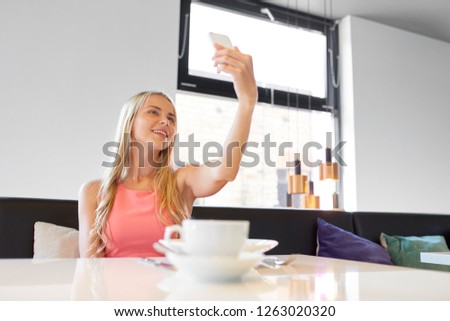 technology and leisure concept - happy woman with smartphone taking selfie at restaurant