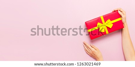 Woman hands holding present red box with gold ribbon on pink background Flat lay top view. Present for birthday, surprise, valentine day, Christmas, New Year. Congratulations background copy space.