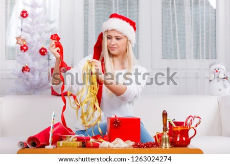 Holiday gifts, seasonal concept. Woman in Santa hat sitting on sofa preparing and packing christmas presents