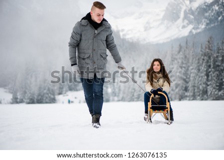 Young man pulling woman on sled in snow