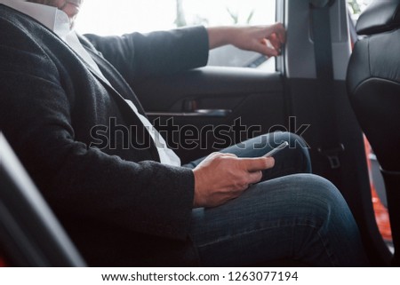 Close up view of businessman holding smartphone while sits on the back seat of the car.