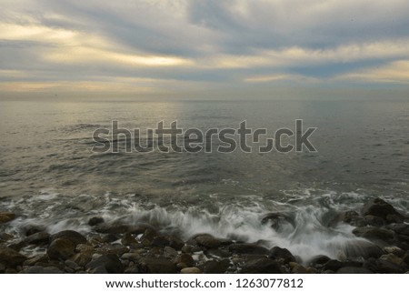 Calm sea with yellow reflections on blue and greenish water. Cloudy day over the sea. Yellow glimpses of the sun. Long exposure photography.