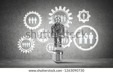 Lightbulb with human from gears inside placed against social gear structure on grey wall. 3D rendering.
