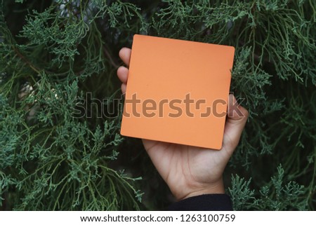 A hand holding orange empty sign board with green abstract background.