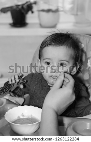 Feeding the baby porridge with a small spoon sitting at the children's table