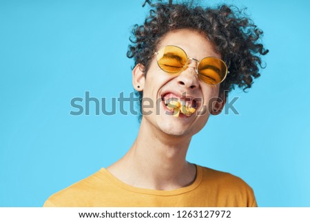 Cheerful man eats pizza and squeezes his eyes in yellow glasses                       