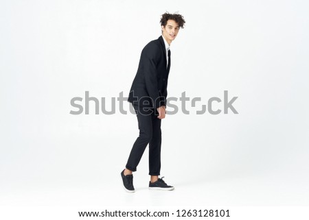 young curly man in black suit and sneakers on a light isolated background                          