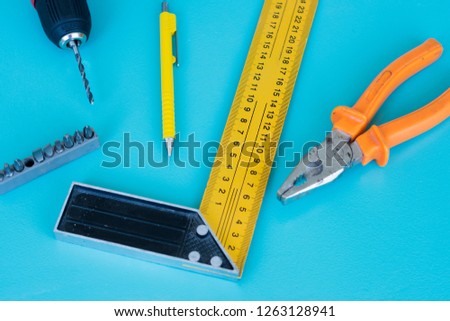 Top view of home construction tools - cordless drill, pencil, drill bit, combination side cutting pliers and  construction carpenter ruler L shape angle square rule on a aqua blue color background.