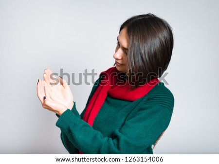 beautiful girl holding something on the palm, red scarf for the New Year and Christmas, close-up over gray background