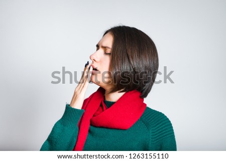 beautiful girl closes a yawning, red scarf for new year and christmas, close-up over gray background
