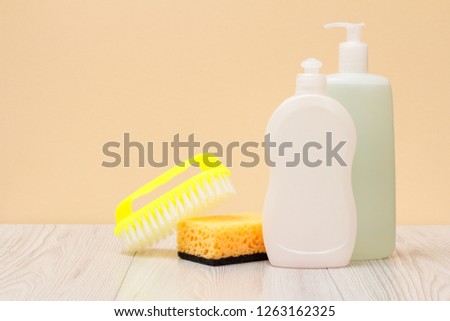 Plastic bottles of dishwashing liquid, glass and tile cleaner, brush and sponge on beige background. Washing and cleaning concept.
