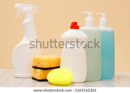 Plastic bottles of dishwashing liquid, glass and tile cleaner, detergent for microwave ovens and stoves, sponges on beige background. Washing and cleaning concept.