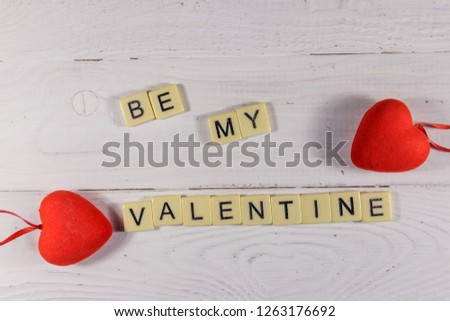 Red hearts and "Be my Valentine" text on white wooden background. Top view
