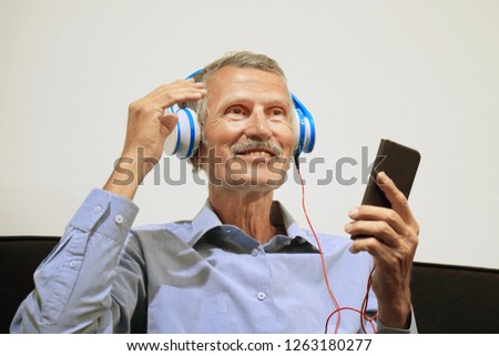 elderly man listen music with headphone. Portrait of a mature smiling man listening music on the black sofa at home