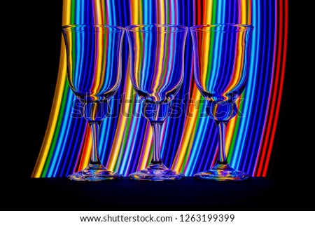 3 elegant empty wine glasses isolated on a black background with colorful red blue yellow and green neon light streaks behind them