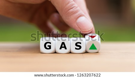 Hand is turning a dice and changes the direction of an arrow symbolizing that the price for gas is changing the trend and goes up instead of down (or vice versa)