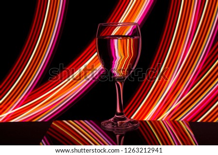 A single wine glass isolated on a black background with red white pink and orange neon light painting streaks of light behind them