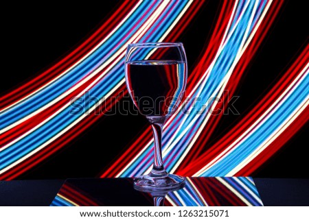 A single wine glass isolated on a black background with colorful red white and blue neon light streaks behind them