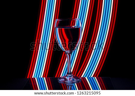 A single wine glass isolated on a black background with colorful red white and blue neon light streaks behind them