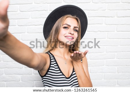 Young woman in straw hat blow kiss while take selfie on phone isolated on brick wall