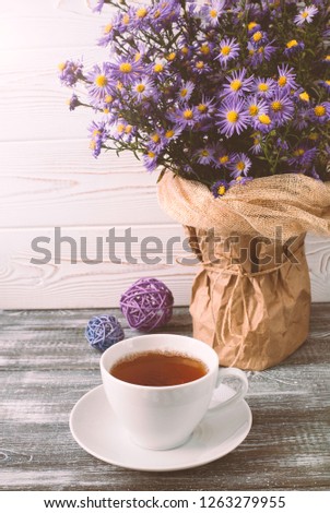 Romantic background with a cup of tea, lilac flowers in a vase on a gray wooden table