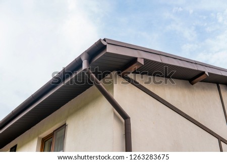 Modern roof covered with tile effect PVC coated brown metal roof sheets against cloudy sky.