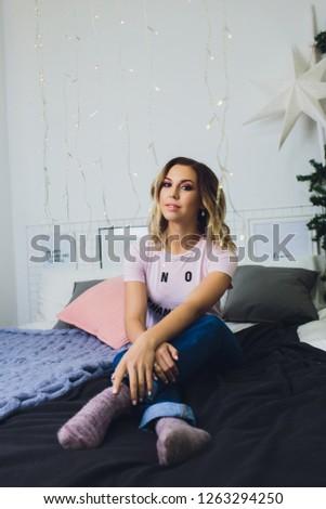 Beautiful woman is sitting in bed at home near christmas tree in cozy interior. Interior with christmas decorations.