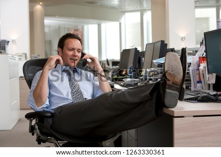 Businessman making phone call in office with feet on desk