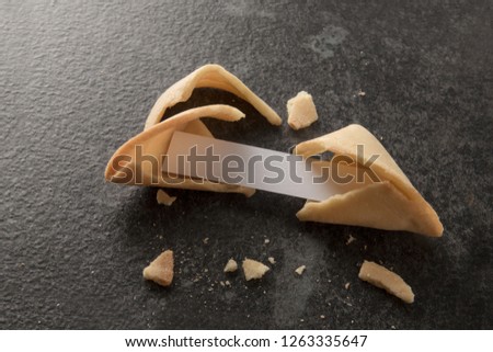 chinese fortune cookies, one is cracked with blank paper slip for the prediction on a dark slate background with copy space