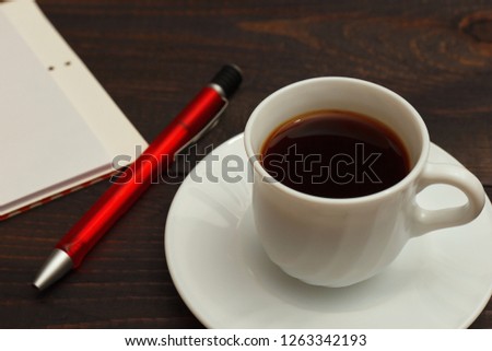 Cup of coffee, pen and notebook on a wooden background