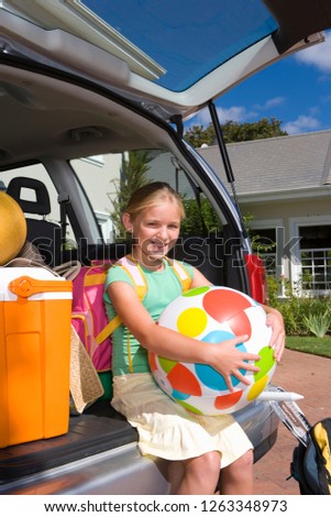 Girl sitting in open boot of car packed with luggage for vacation