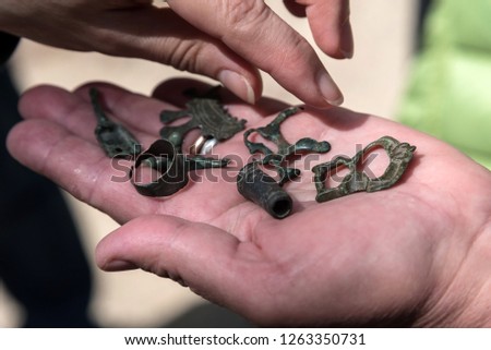 The concept is a treasure hunt. On the hand is an old copper ring and other items. Close-up, blurred background. Illuminated by the sun.
